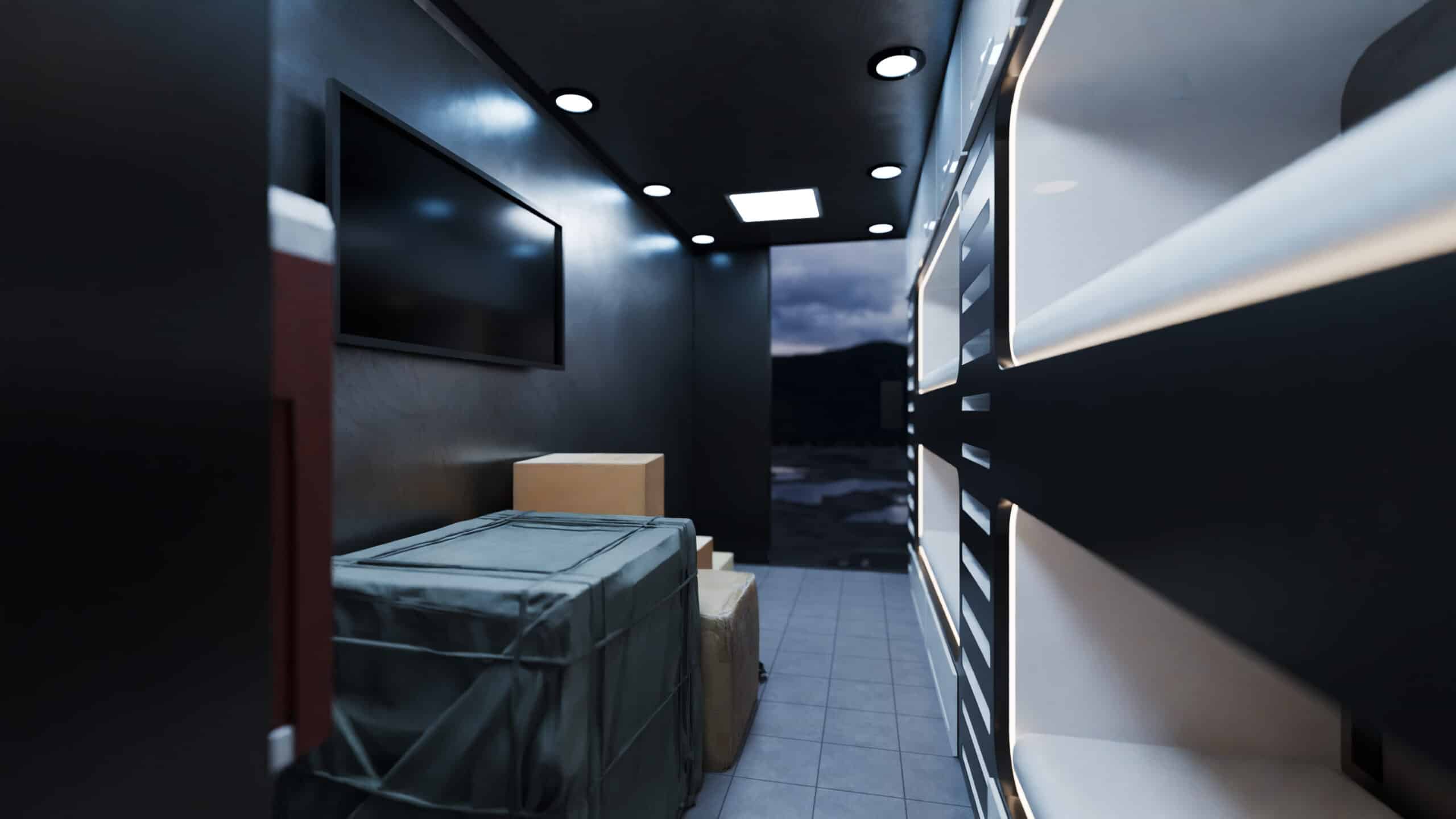 Interior of a solar-powered trailer designed for disaster relief, showing compact sleeping pods along one wall, storage boxes, overhead lighting, and a mounted display screen, with the rear door open to an outdoor view.